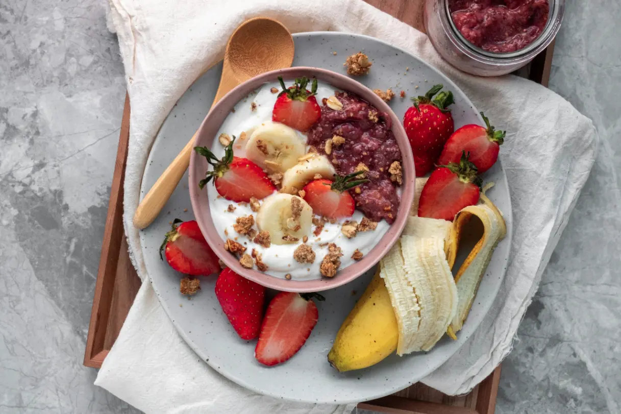 Eine Schüssel mit pflanzlichem Joghurt, unterschiedlichen Beeren, Banane, Beerenmus, dem HAFERVOLL Flapjack Berry & Cashew, Leinsamen und Agavendicksaft.