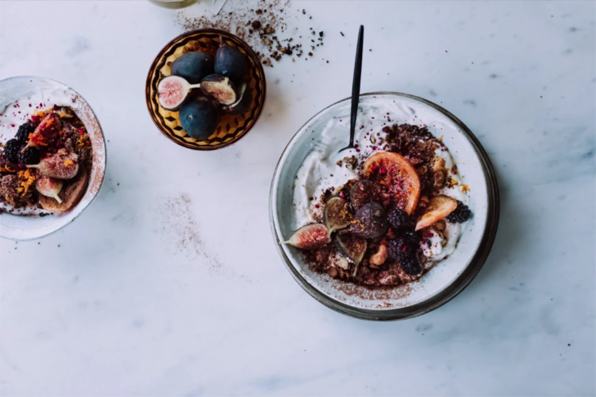 Eine Schüssel mit pflanzlichem Vanillejoghurt, Feigen, HAFERVOLL Flapjack Cocoa Nib & Hazelnut, Brombeeren, Kakaonibs und Ahornsirup.