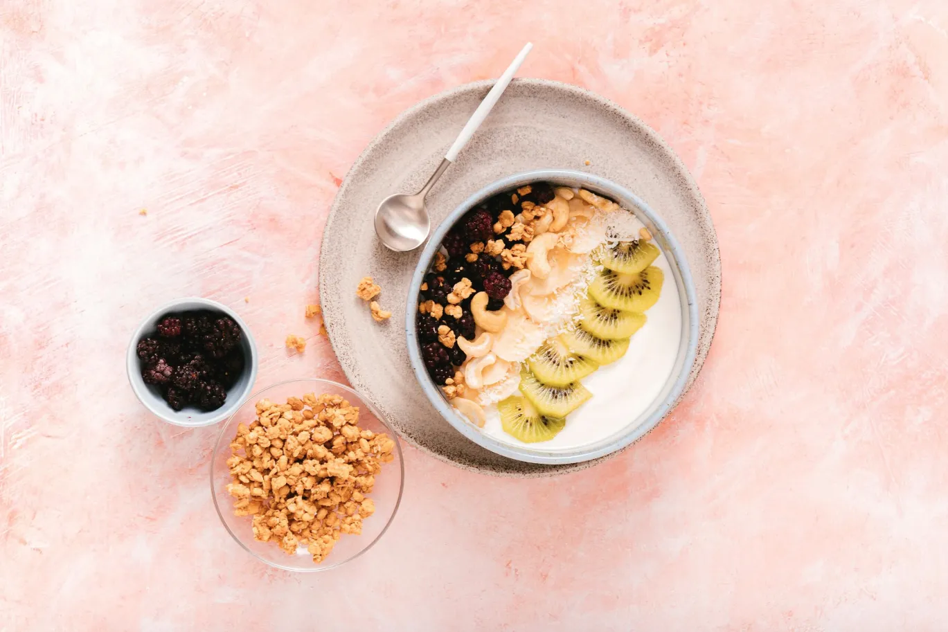 Eine Schüssel mit pflanzlichem Joghurt, Banane, Kiwi, Brombeeren, HAFERVOLL Flapjack Banana & Brazil Nut, Cashews, Ahornsirup und Kokosraspeln.